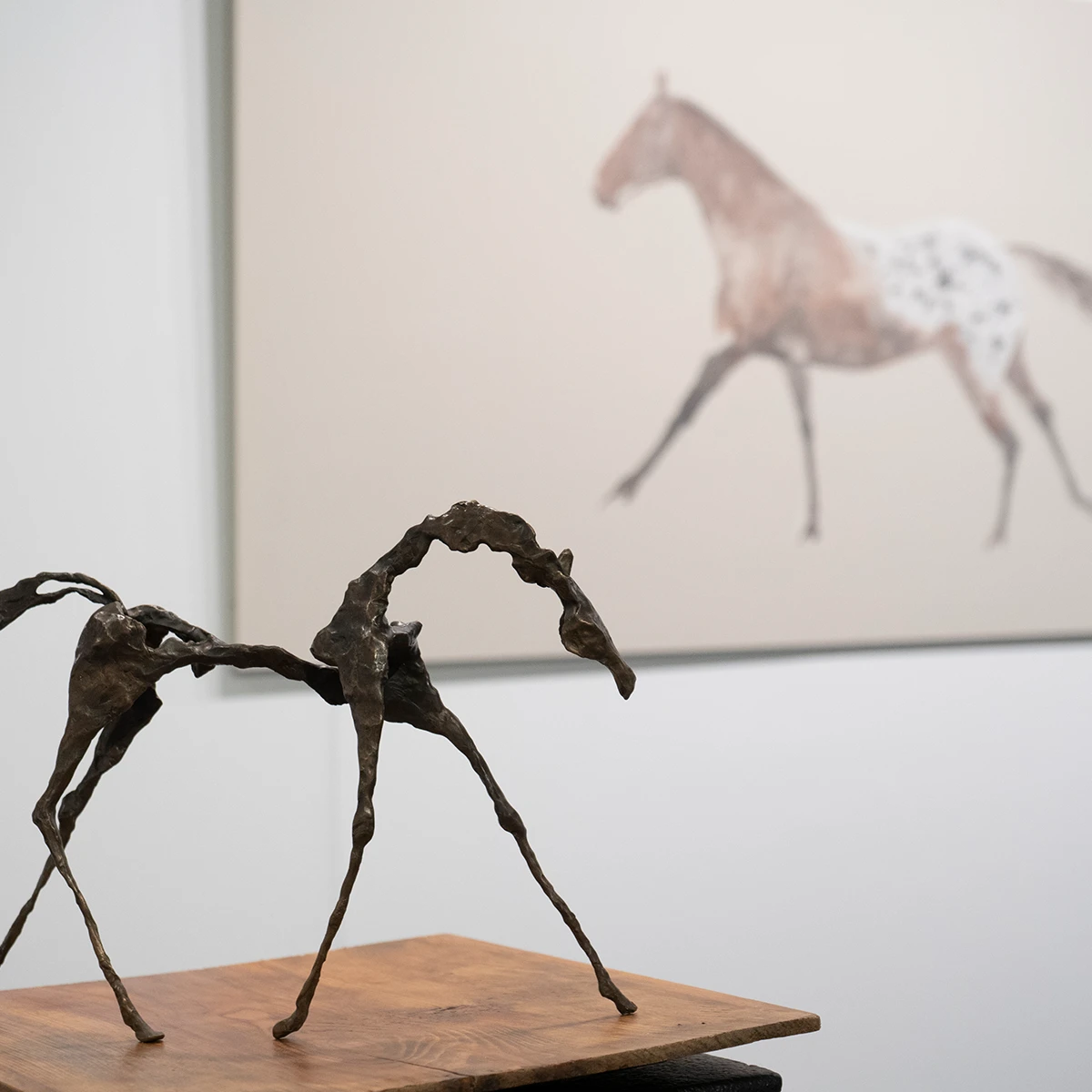 escultura de caballo en metal con cuadro ecuestre de fondo