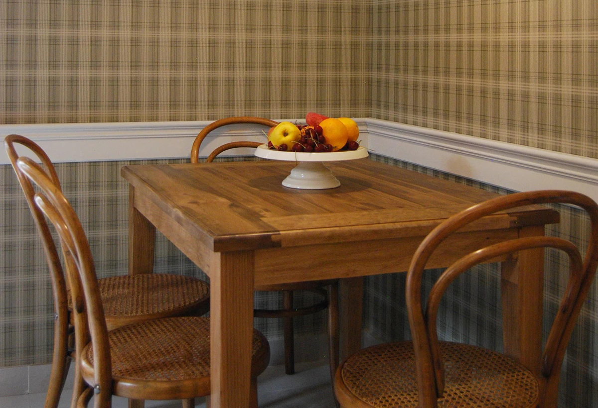 mesa de madera con centro de frutas, al fondo pared con papel a cuadros