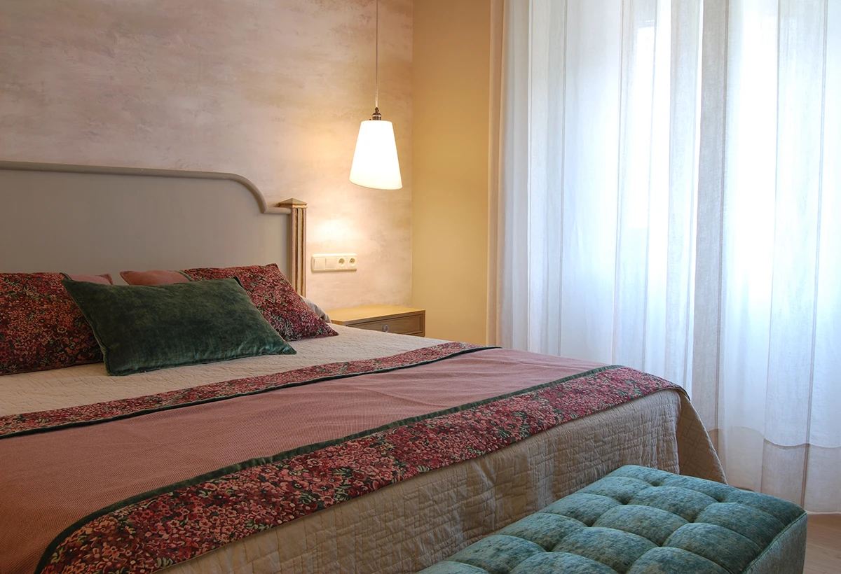 cama de habitación de hotel con mueble tapizado verde a los pies de la cama
