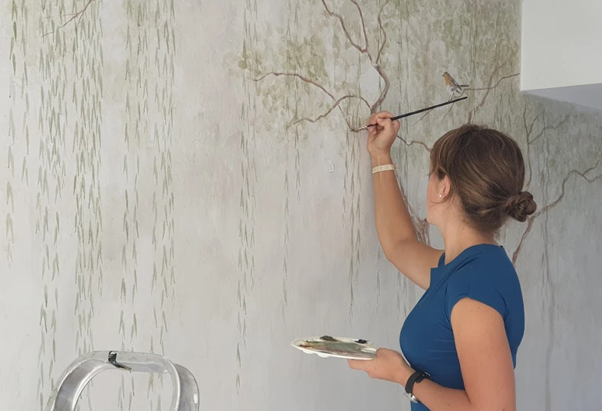 mujer pintando a mano mural de pared con sauce
