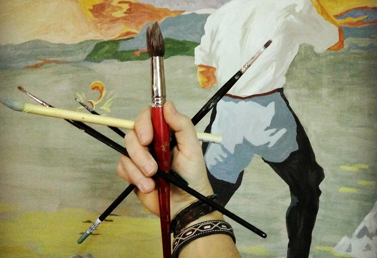 detalle de mano agarrando pinceles con mural de fondo